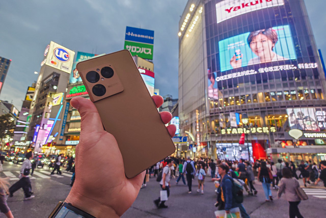 渋谷スクランブル交差点の夜景を背景にXperia 1 VIII ネイティブゴールドを手に持ってBluetooth通信テストを行った様子